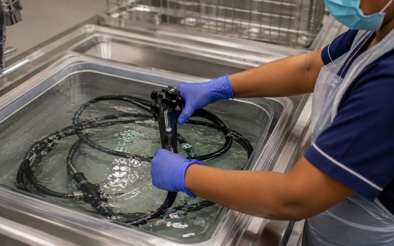 Indian nurse submerging a flexible endoscope into a basin of glutaraldehyde